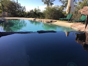 A clear swimming pool with rock formations around it, surrounded by greenery and a few lounge chairs. - Amamoor Lodge (Amamoor)