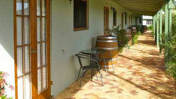 A covered outdoor area with a brick floor, wooden barrels, metal chairs, and a row of windows.