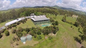 An aerial view of a property with a large building, a swimming pool, and two green water tanks. - Amamoor Lodge (Amamoor)