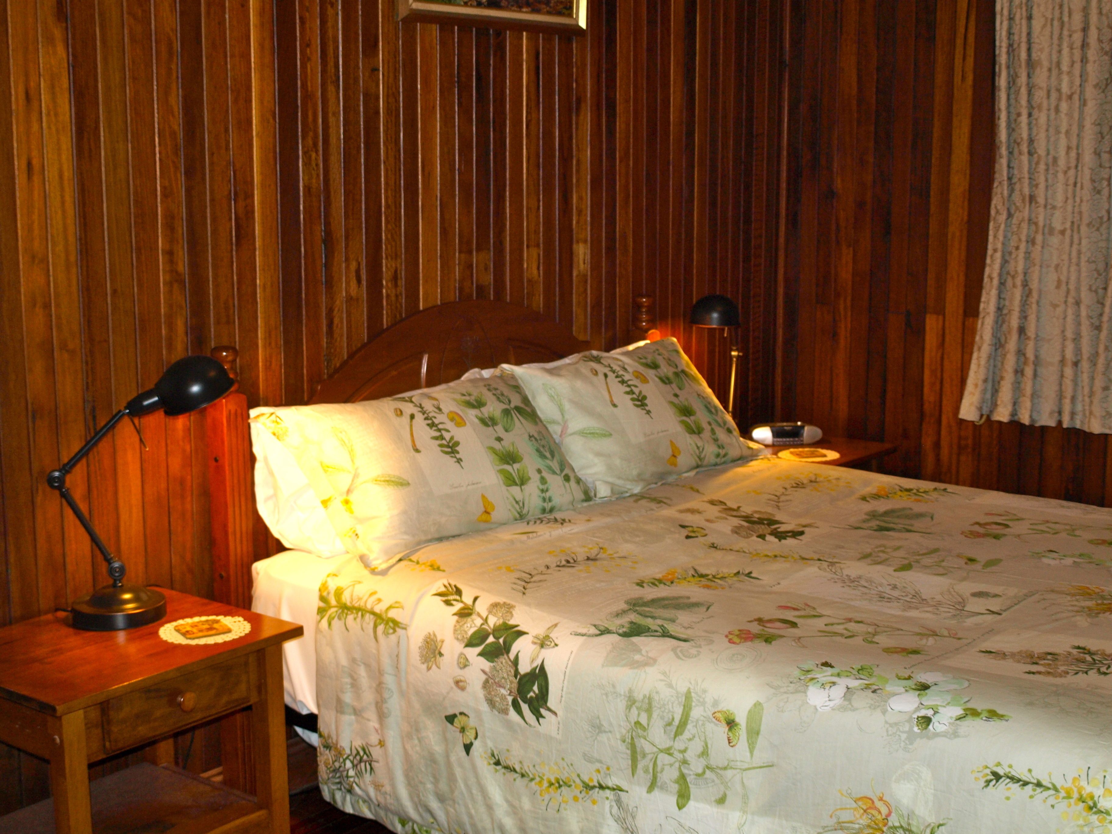A wooden-paneled room with a bed, two bedside lamps, and a nightstand with a lamp.