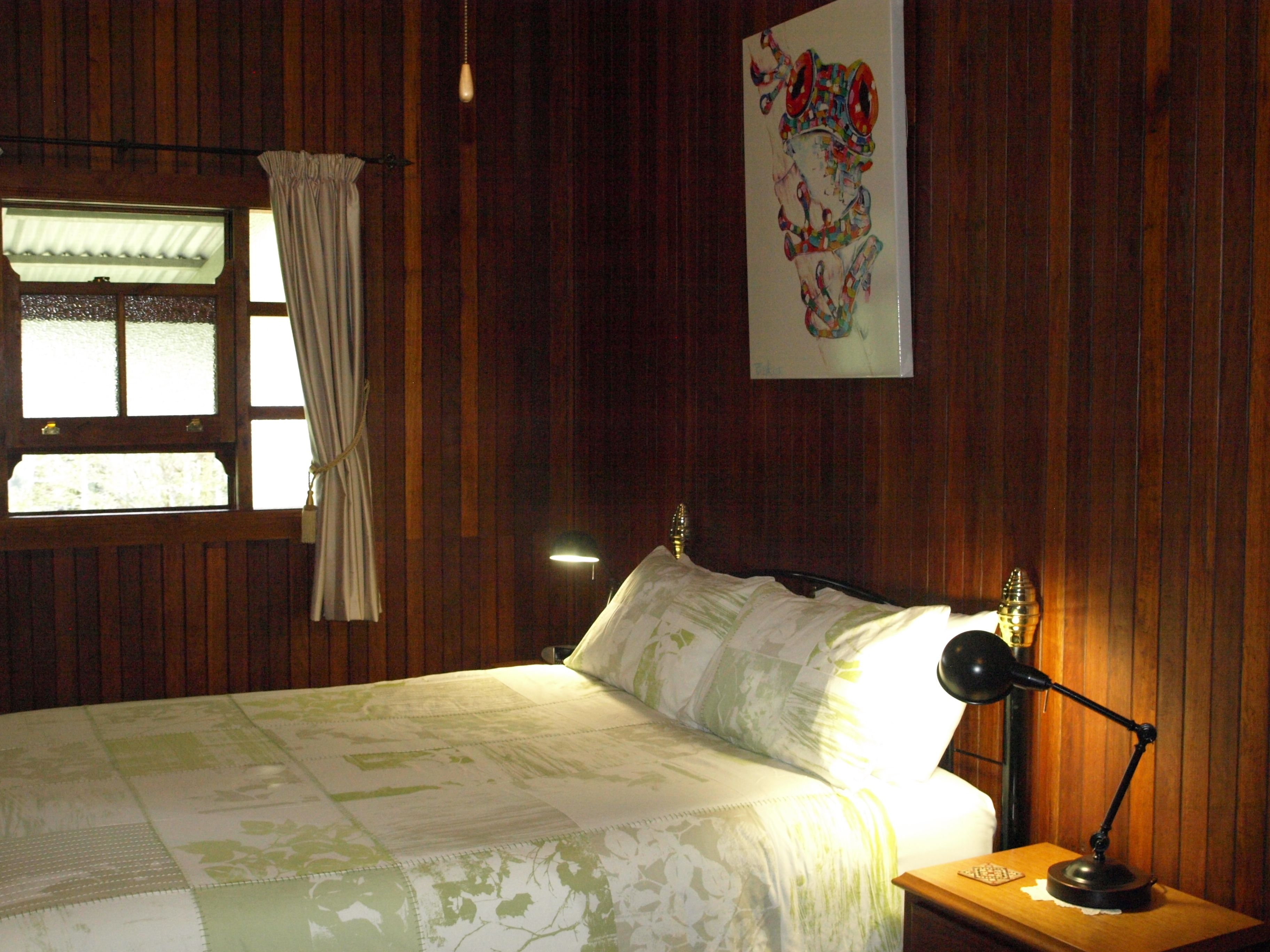 Una stanza con rivestimento in legno, un letto, un comodino, una lampada e una finestra con tende.