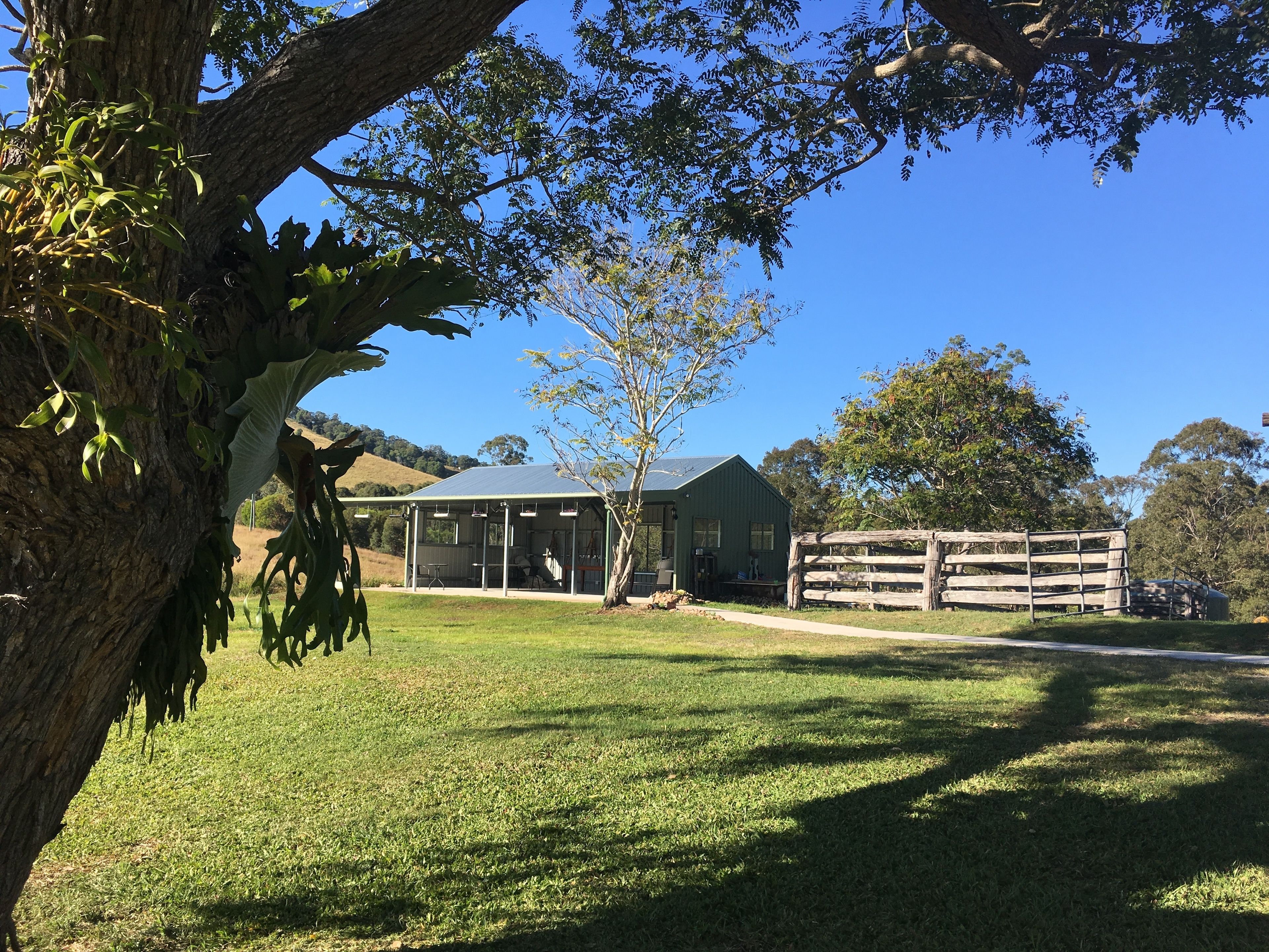 A green building with a covered outdoor area, surrounded by trees and a grassy field.