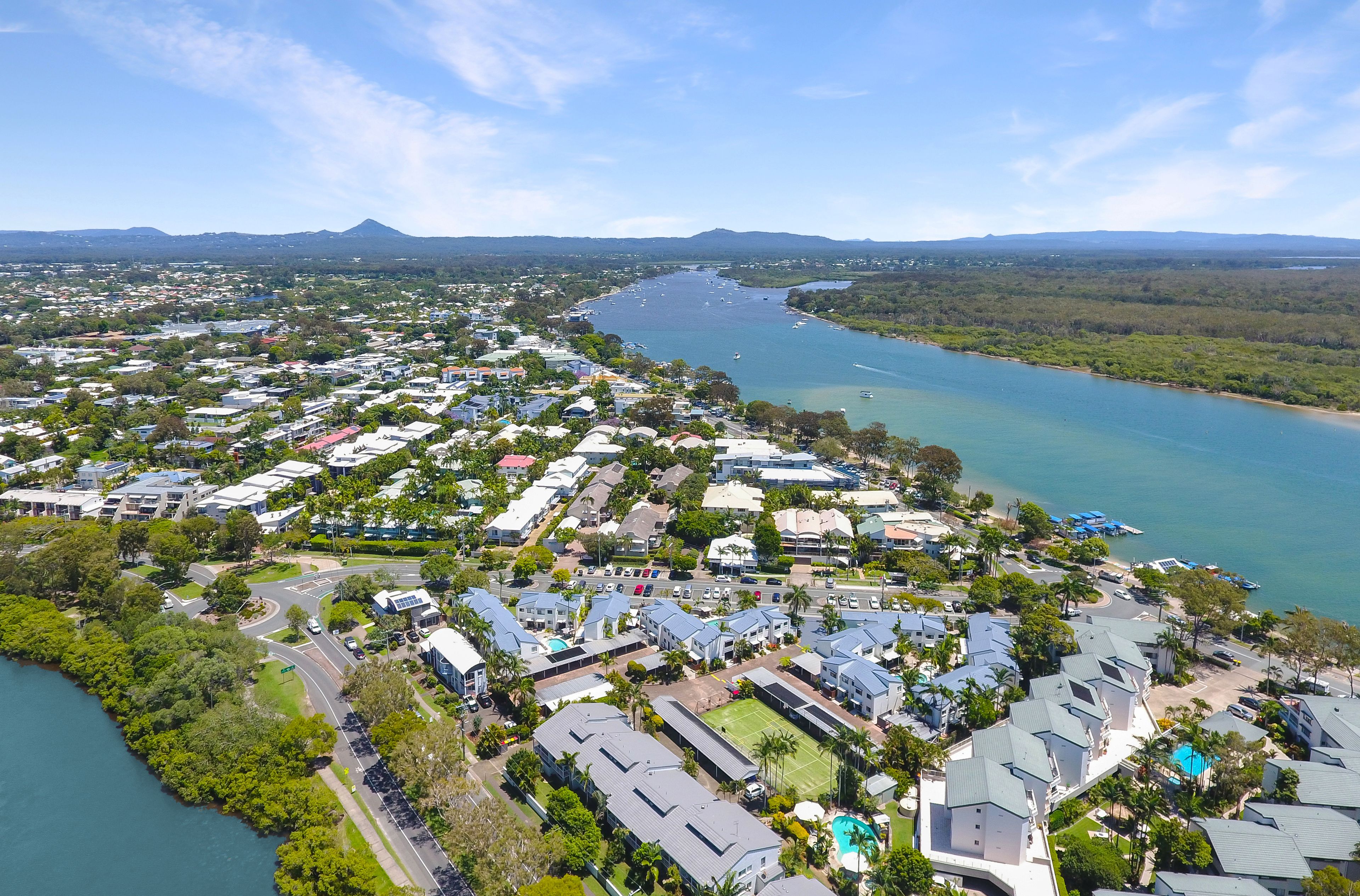 An aerial view of a coastal residential area with houses, a road, and a river.