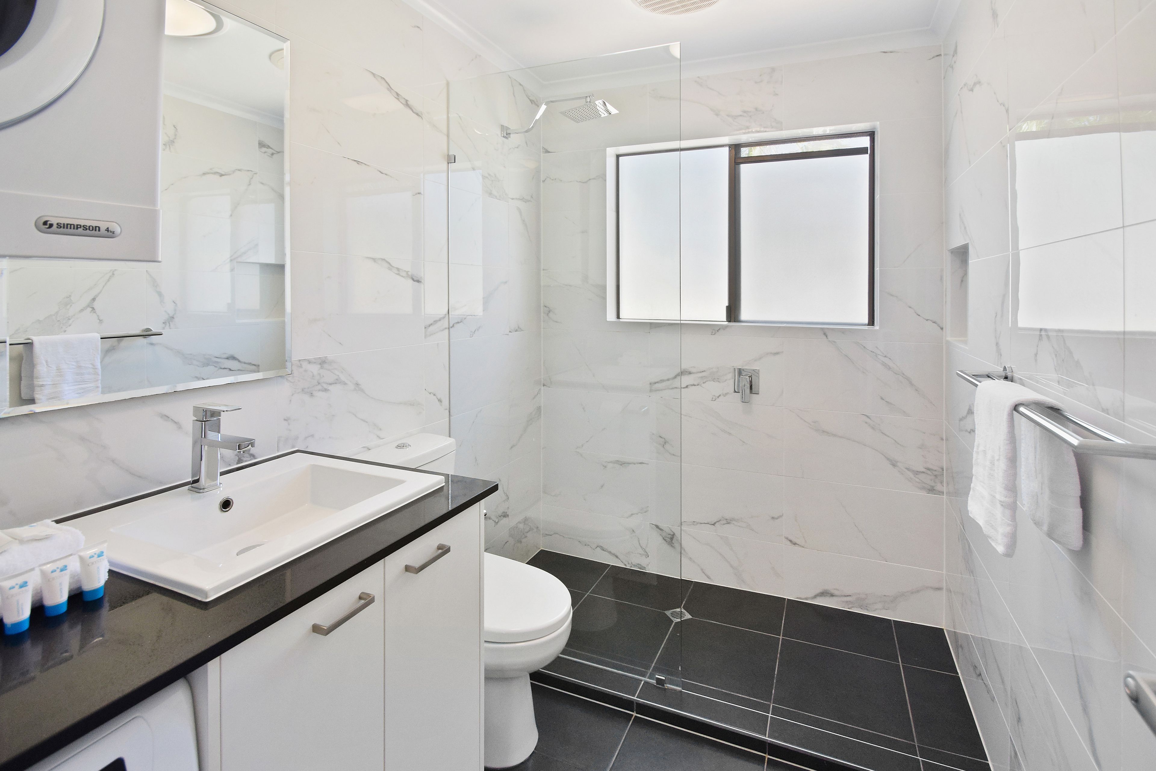 A modern bathroom with a white sink, black countertop, and a glass-enclosed shower.