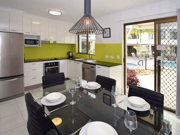 Una cocina moderna con armarios blancos, un refrigerador de acero inoxidable y un microondas. Hay una mesa de comedor puesta con platos, vasos y cubiertos.