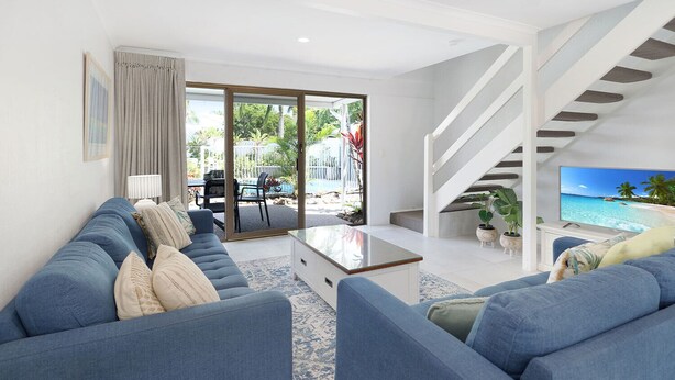 Una sala de estar moderna con un conjunto de sofá, una mesa de centro y un televisor mostrando una escena de playa.