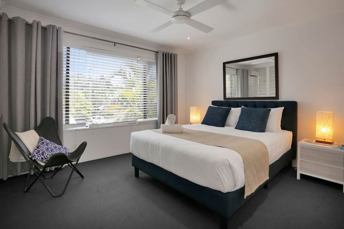 A modern hotel room with a large bed, a chair, a nightstand, and a ceiling fan.