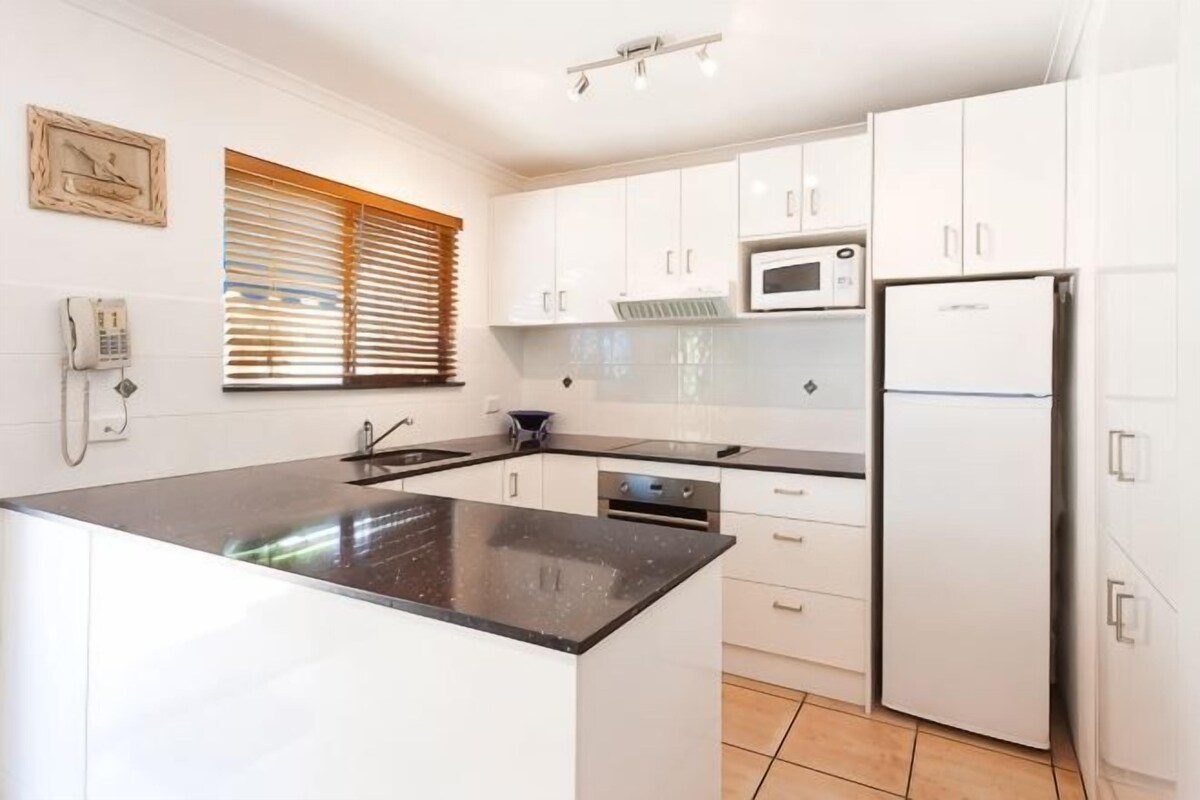 A kitchen with white cabinets, a black countertop, a microwave, and a refrigerator.