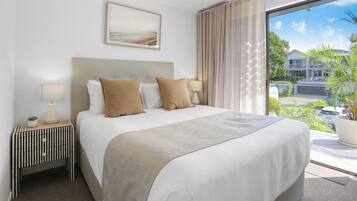 Habitación de hotel con una cama grande, una mesita de noche con lámpara, un cuadro en la pared y vistas al exterior.