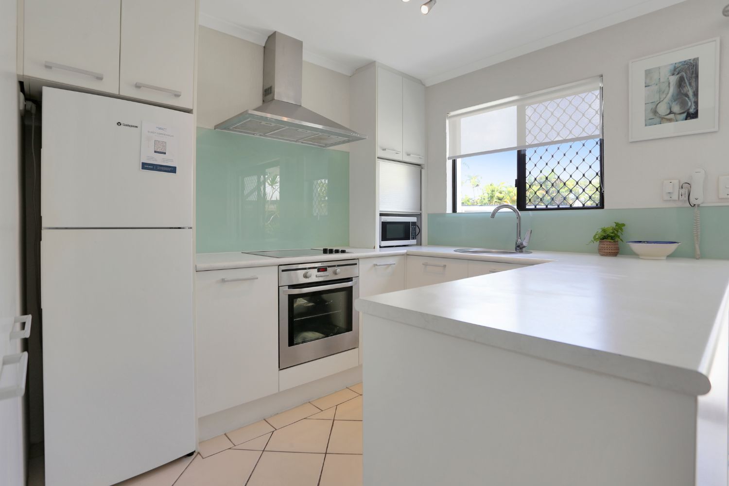 A modern kitchen with white cabinetry, a stainless steel range hood, a built-in oven, a microwave, and a large island with a sink.