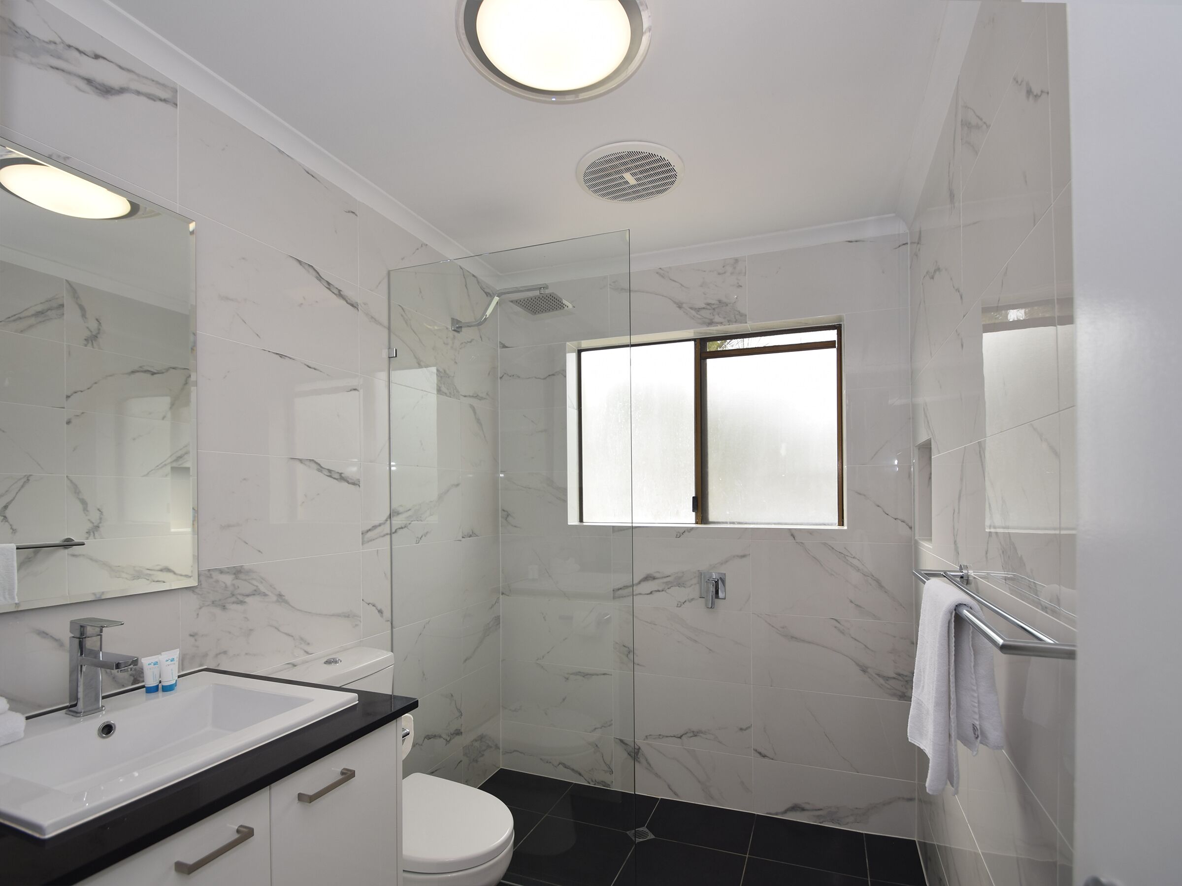 A modern bathroom with a marble floor, a glass shower enclosure, a white toilet, and a sink with a black countertop.