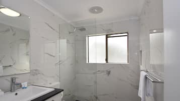 A modern bathroom with a marble floor, a glass shower enclosure, a white toilet, and a sink with a black countertop.