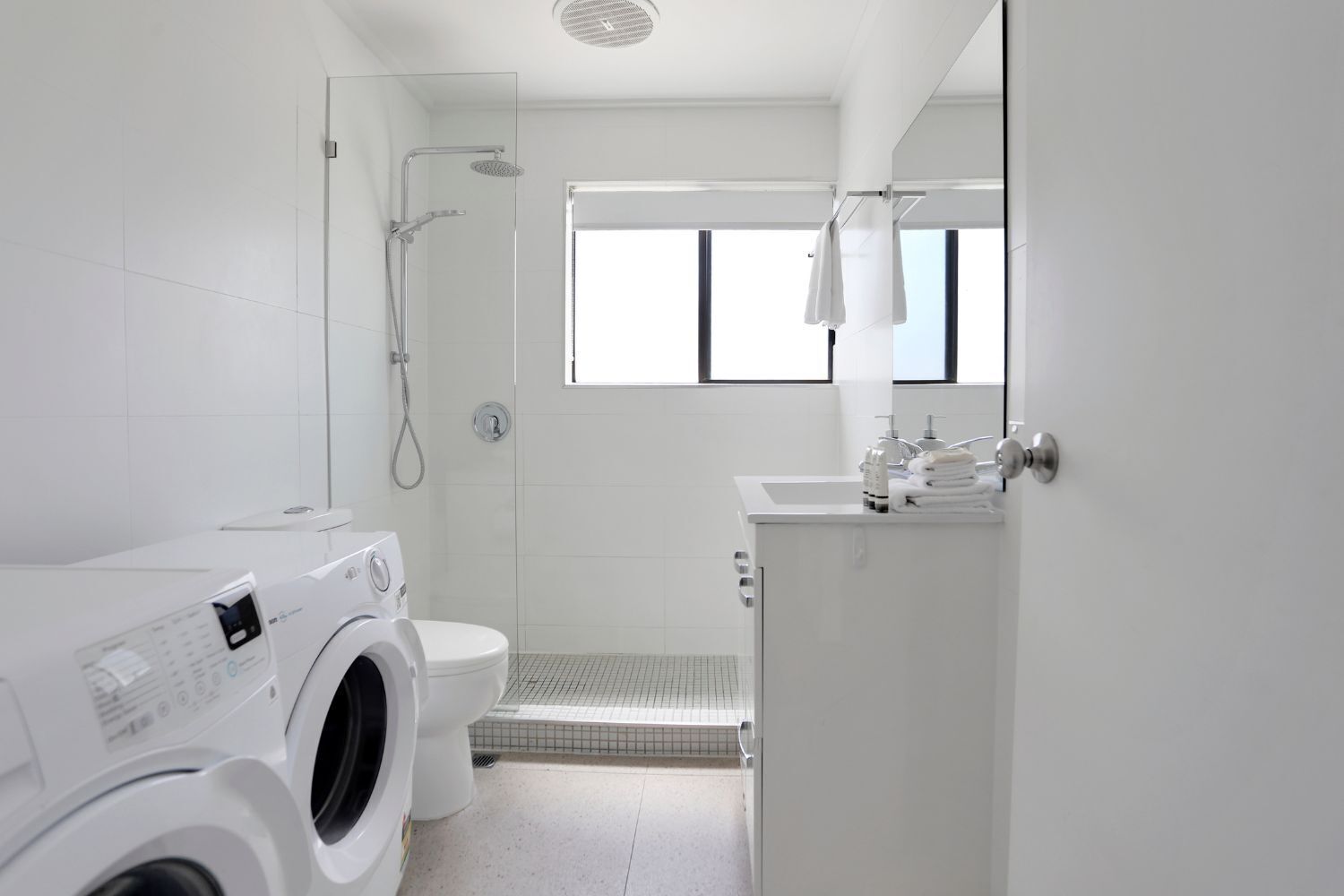 Une salle de bain moderne équipée d’un lave-linge, de toilettes, d’une douche et d’un lavabo.