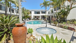 Zona de piscina con jacuzzi, rodeada de palmeras y una gran maceta de terracota.