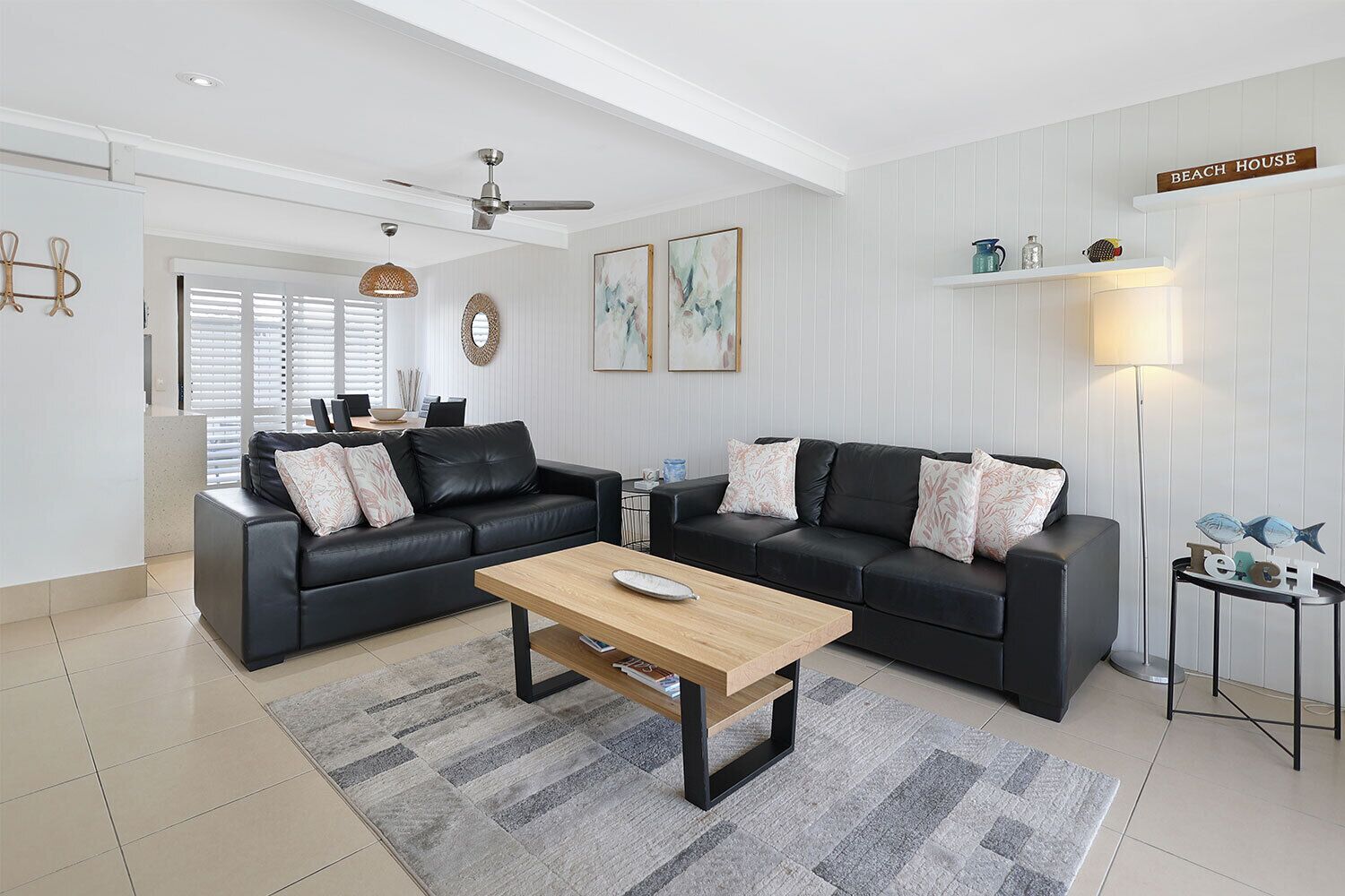 A modern living room with two black leather sofas, a wooden coffee table, and a grey striped rug.