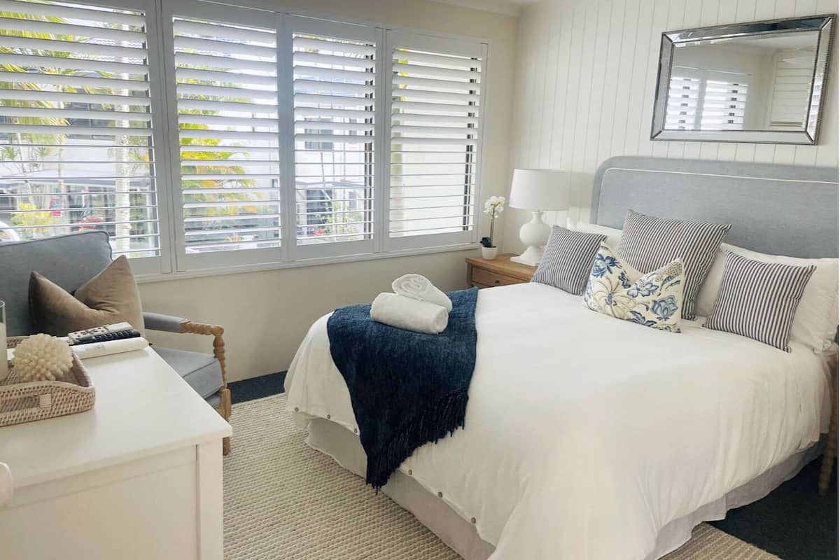 A hotel room with a bed, a chair, a desk, and a window with blinds.