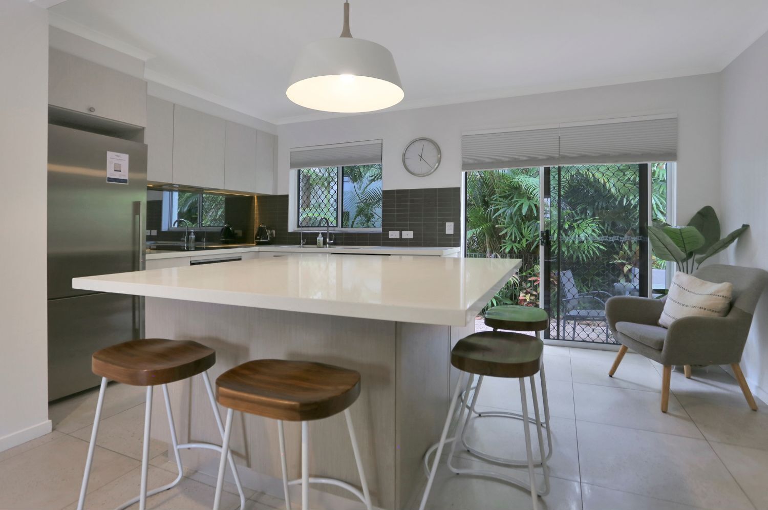 A modern kitchen with a large island, stainless steel appliances, and a dining area with a chair and stools.
