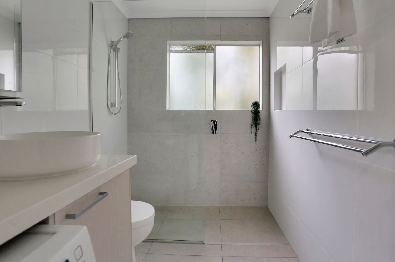 Et moderne badeværelse med en stor vask, toilet, brusebad og et vindue.