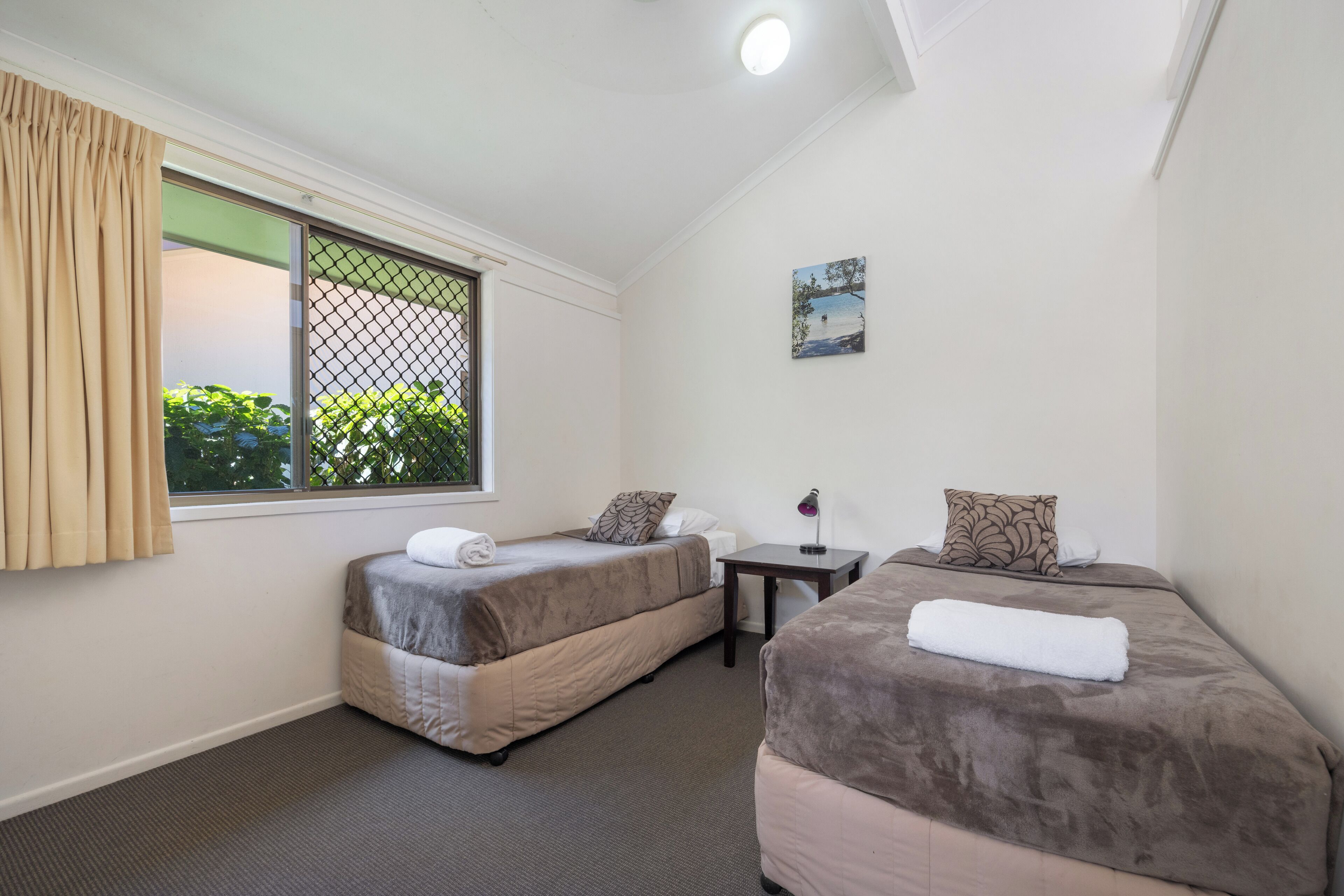 A room with two beds, a small table, and a window with curtains.