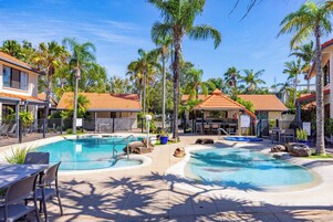 Uma área de piscina com duas piscinas separadas, palmeiras e mobiliário para áreas externas.