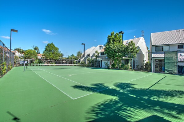 A tennis court with a net, surrounded by trees and buildings. - Nautilus Noosa Holiday Resort (Noosaville)