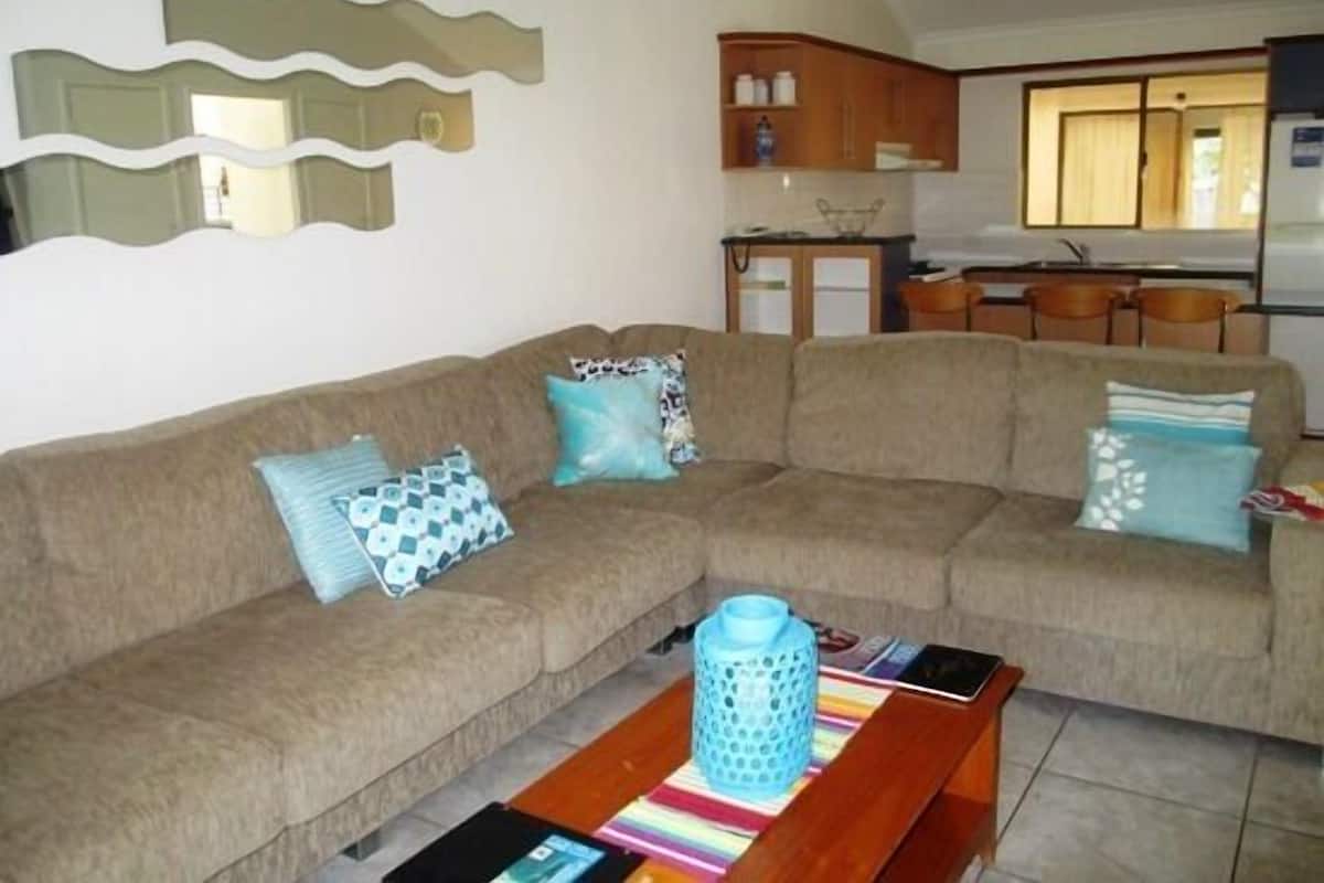A living room with a sofa, a coffee table, and a kitchen in the background.
