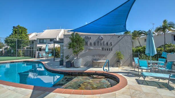 Una piscina con borde de piedra, sillas de descanso y una zona sombreada con toldo azul.