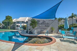A swimming pool with a stone edge, lounge chairs, and a shaded area with a blue canopy. - Nautilus Noosa Holiday Resort (Noosaville)