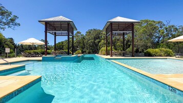 A swimming pool with two gazebos, surrounded by lounge chairs and umbrellas.