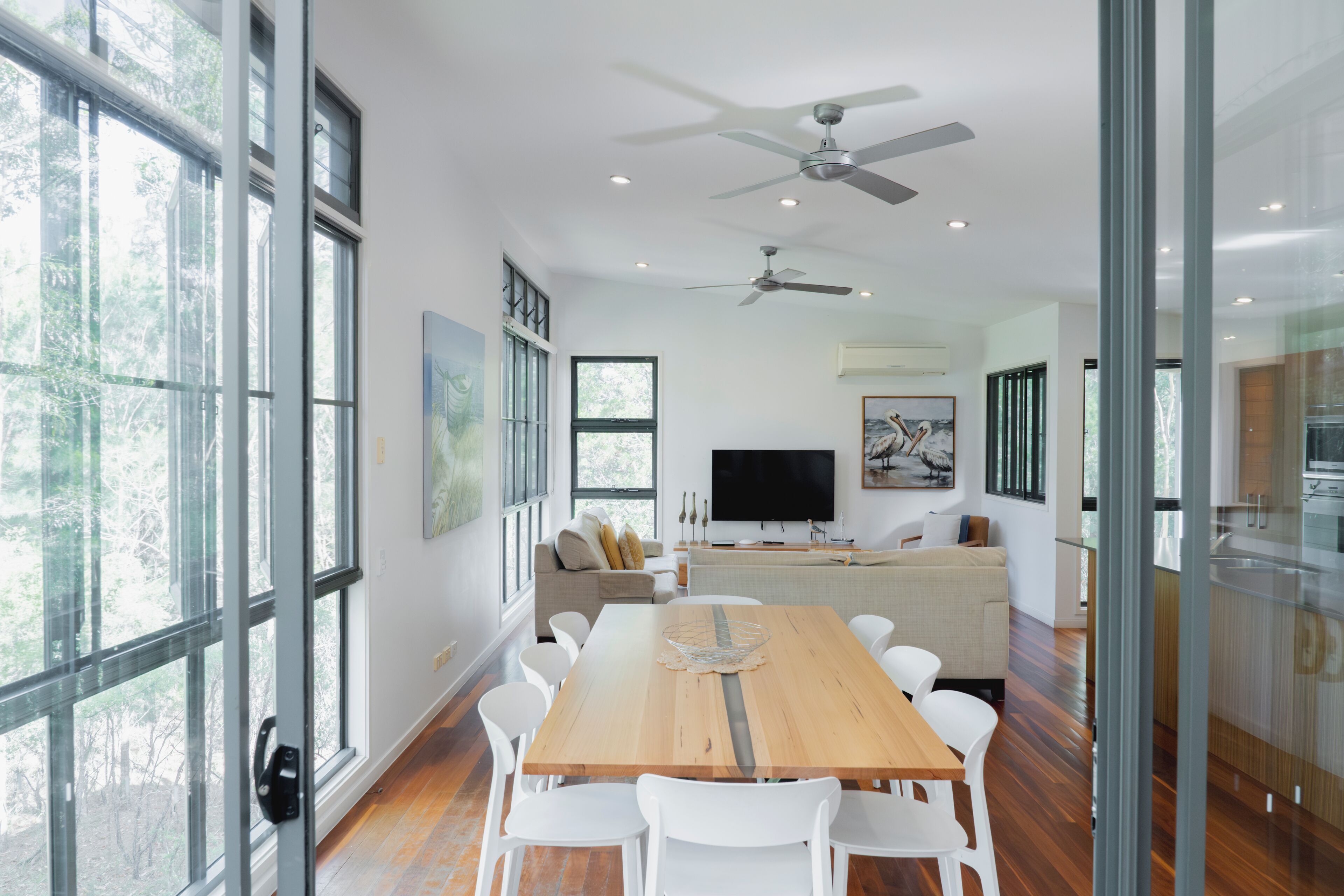 A modern dining area with a wooden table, white chairs, and a ceiling fan.