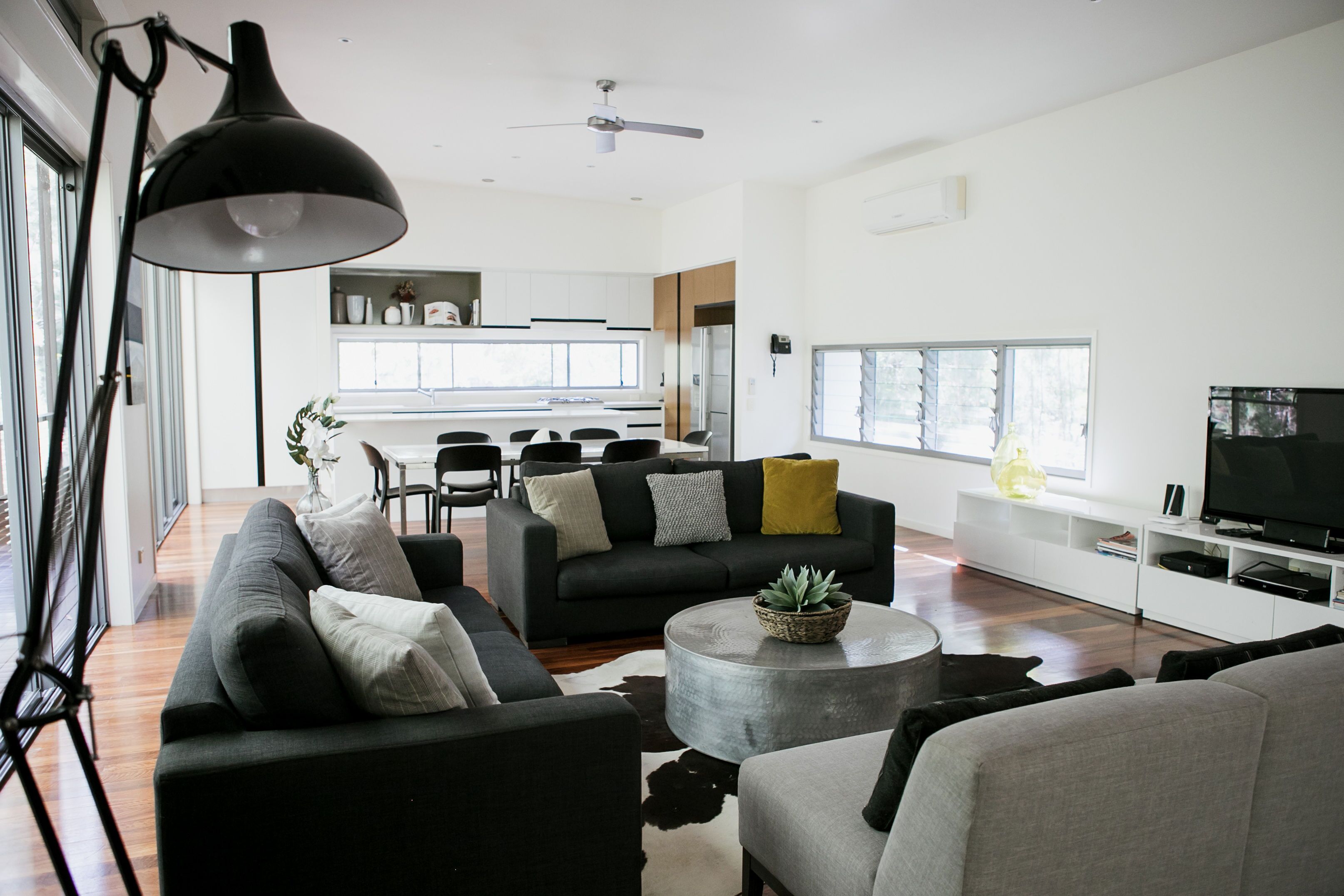 Una sala de estar moderna con sofá, mesa de centro y televisor. Se observa un comedor con sillas y una mesa al fondo.