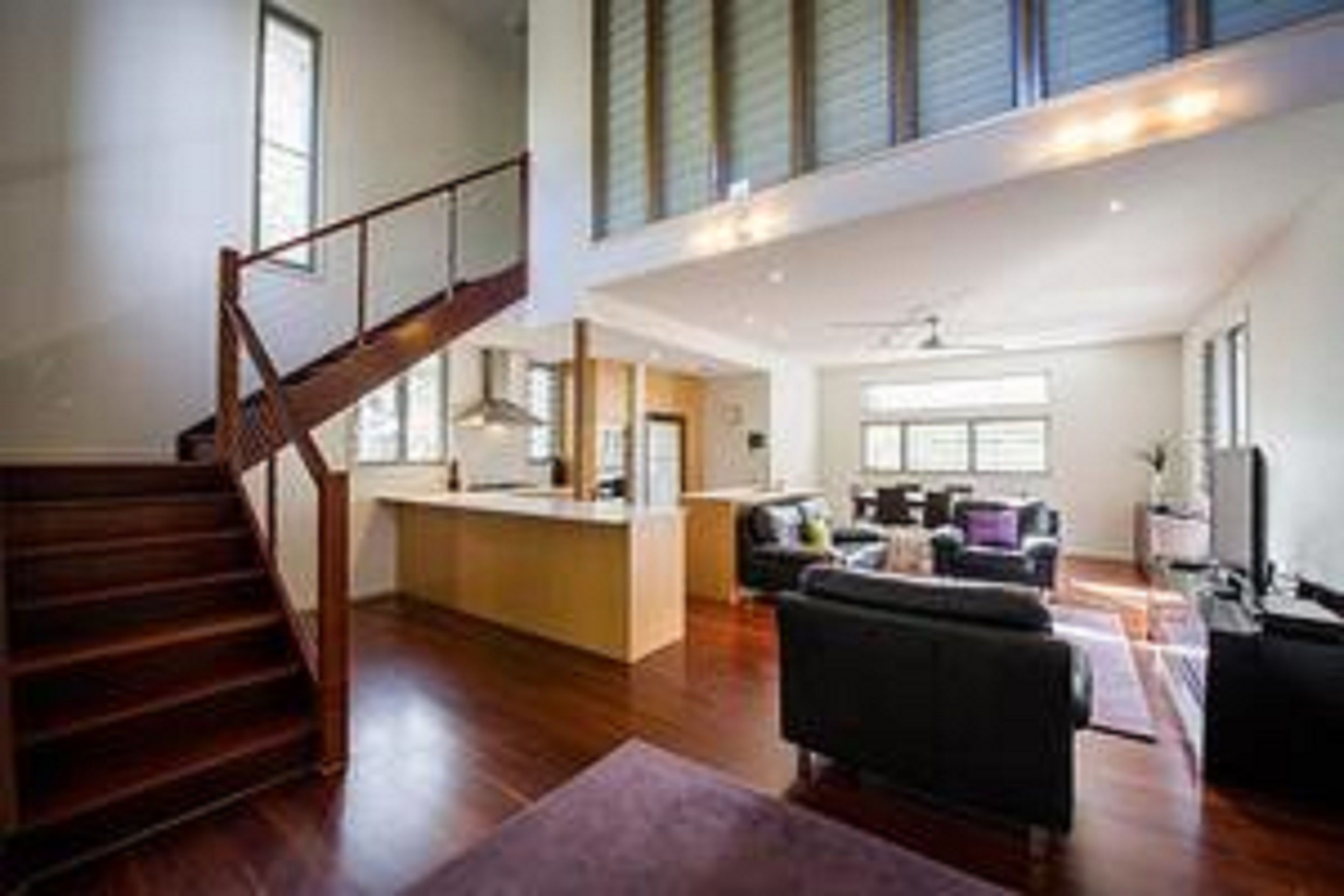 Un vaste espace de vie comprenant un escalier en bois, un îlot de cuisine et un coin salon avec un canapé et des fauteuils.