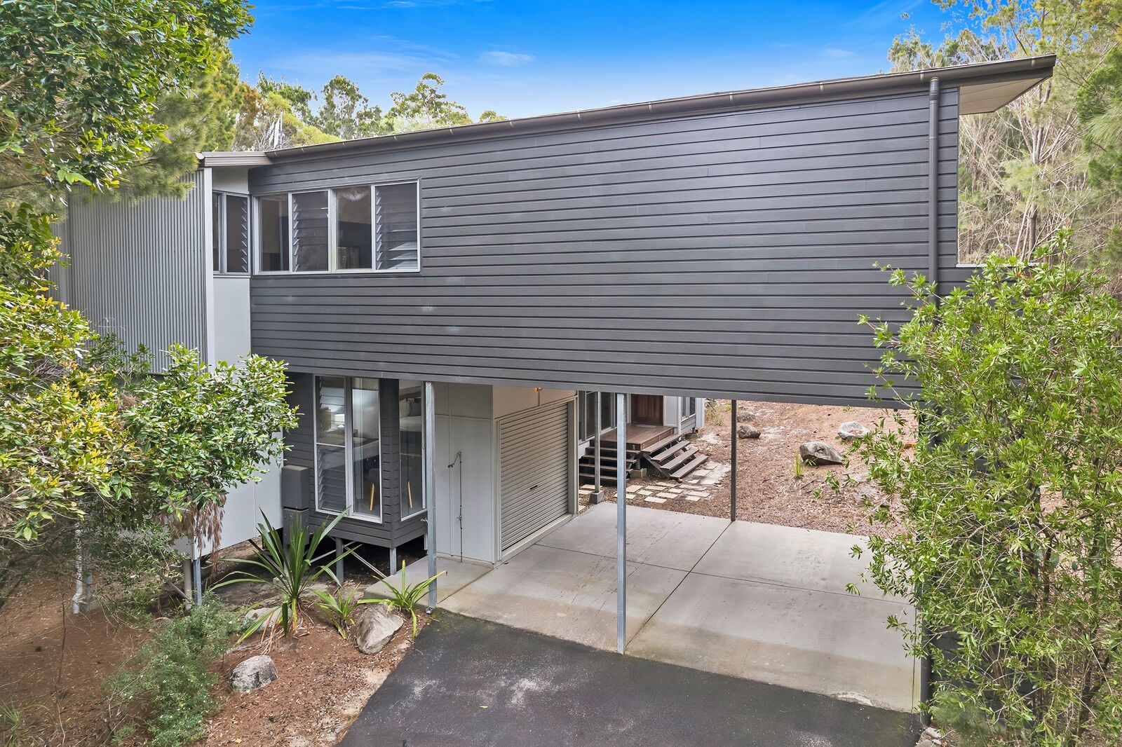 A modern two-story house with a flat roof, large windows, and a covered outdoor area.