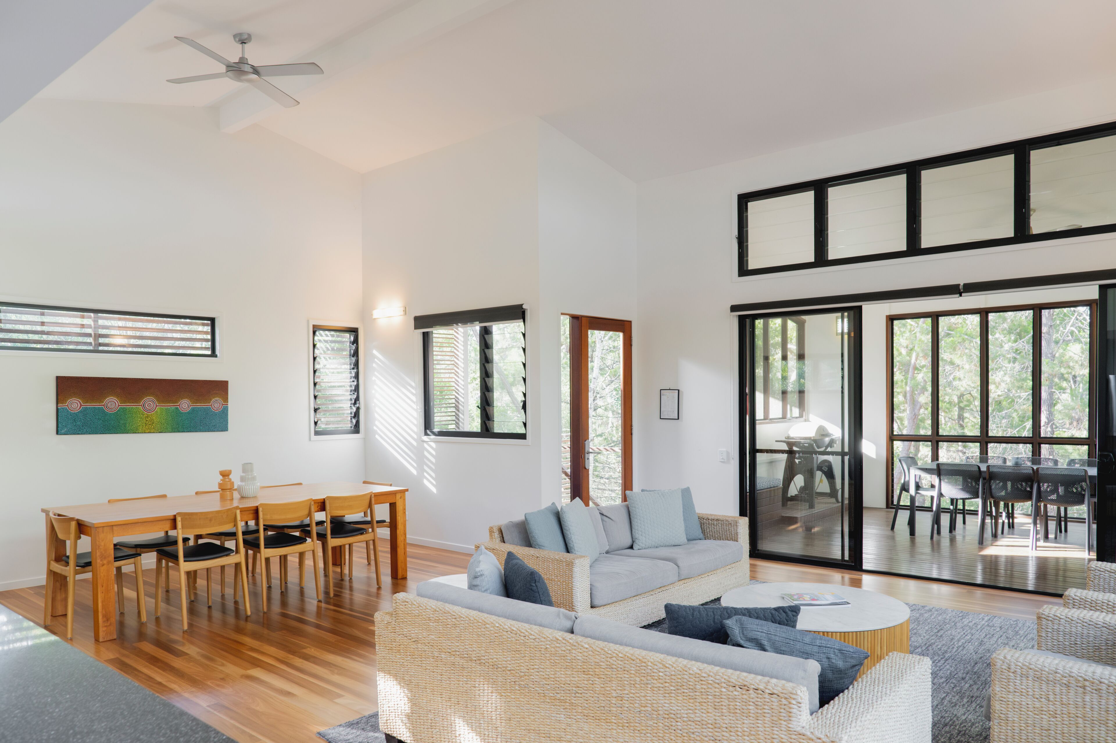 A spacious living area with a dining table, sofas, and a large sliding glass door leading to an outdoor patio.