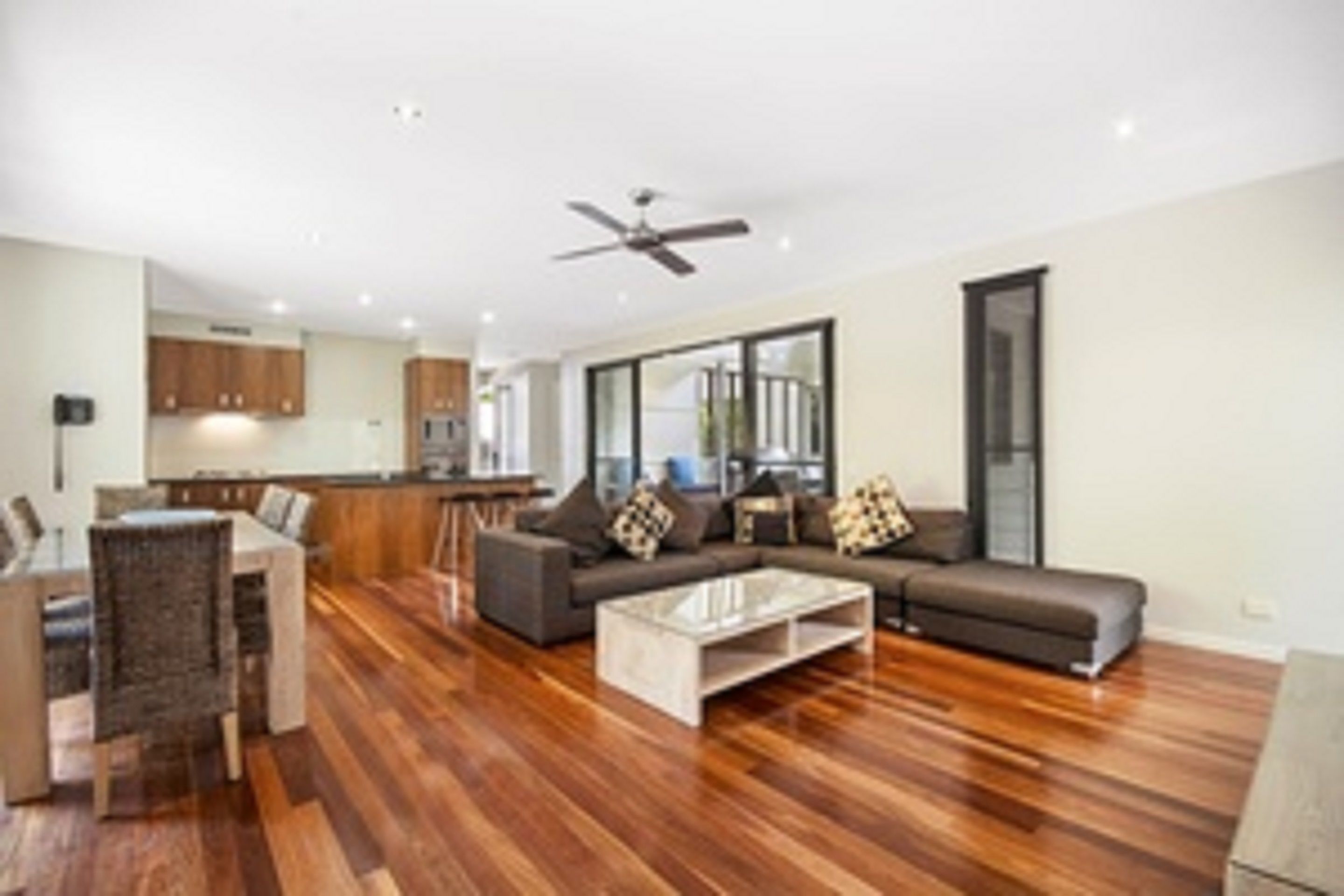 A modern living room with a dining area, wooden flooring, and a ceiling fan.