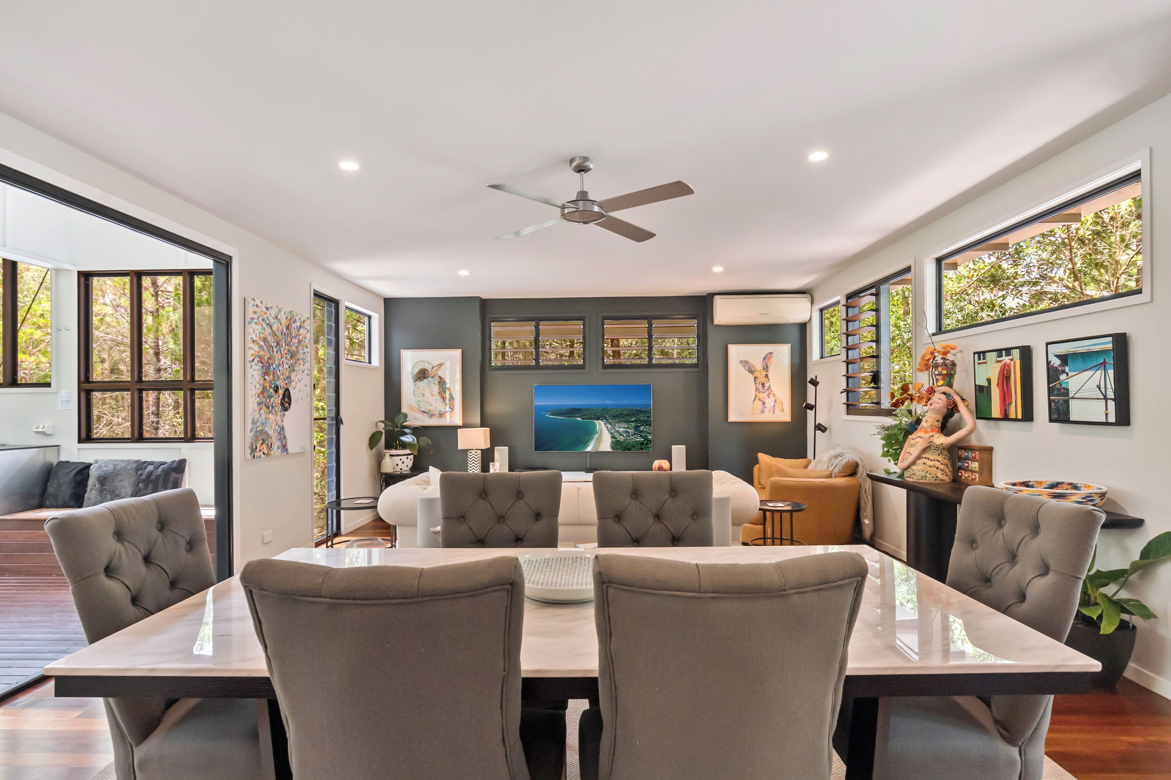 A modern dining area with a large table, comfortable chairs, and a ceiling fan.
