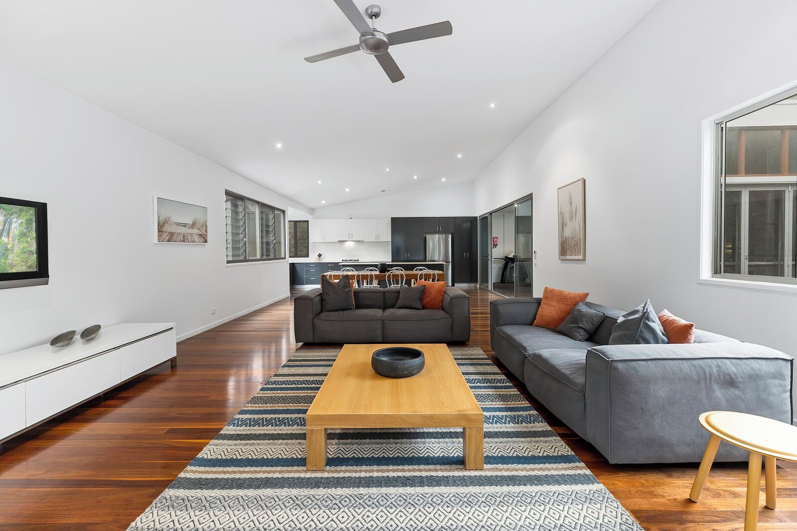 A spacious living area with a large sofa, a coffee table, and a TV mounted on the wall.