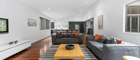 A spacious living area with a large sofa, a coffee table, and a TV mounted on the wall.