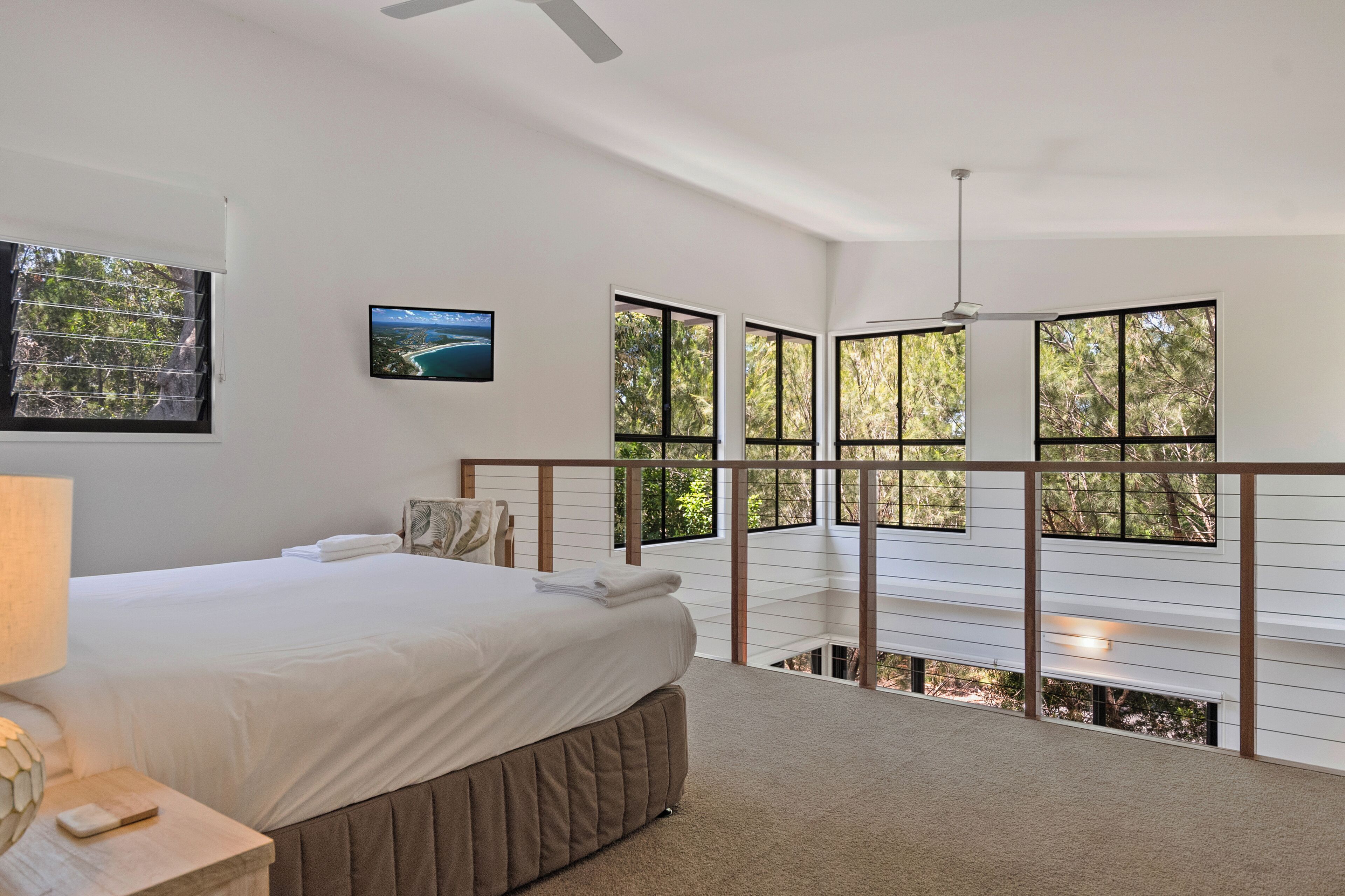 A bedroom with a bed, a TV, and large windows overlooking greenery.
