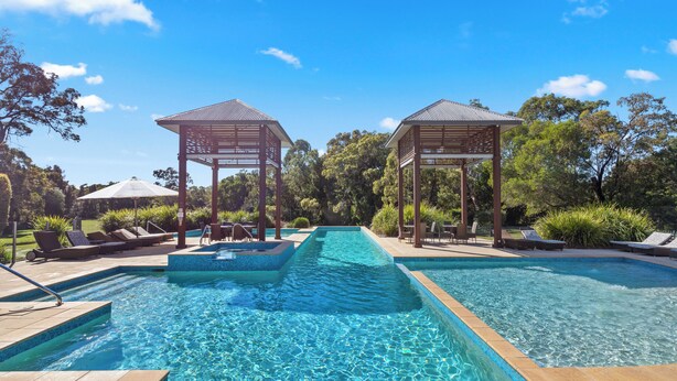 A swimming pool with two wooden gazebos, lounge chairs, and a clear blue sky.