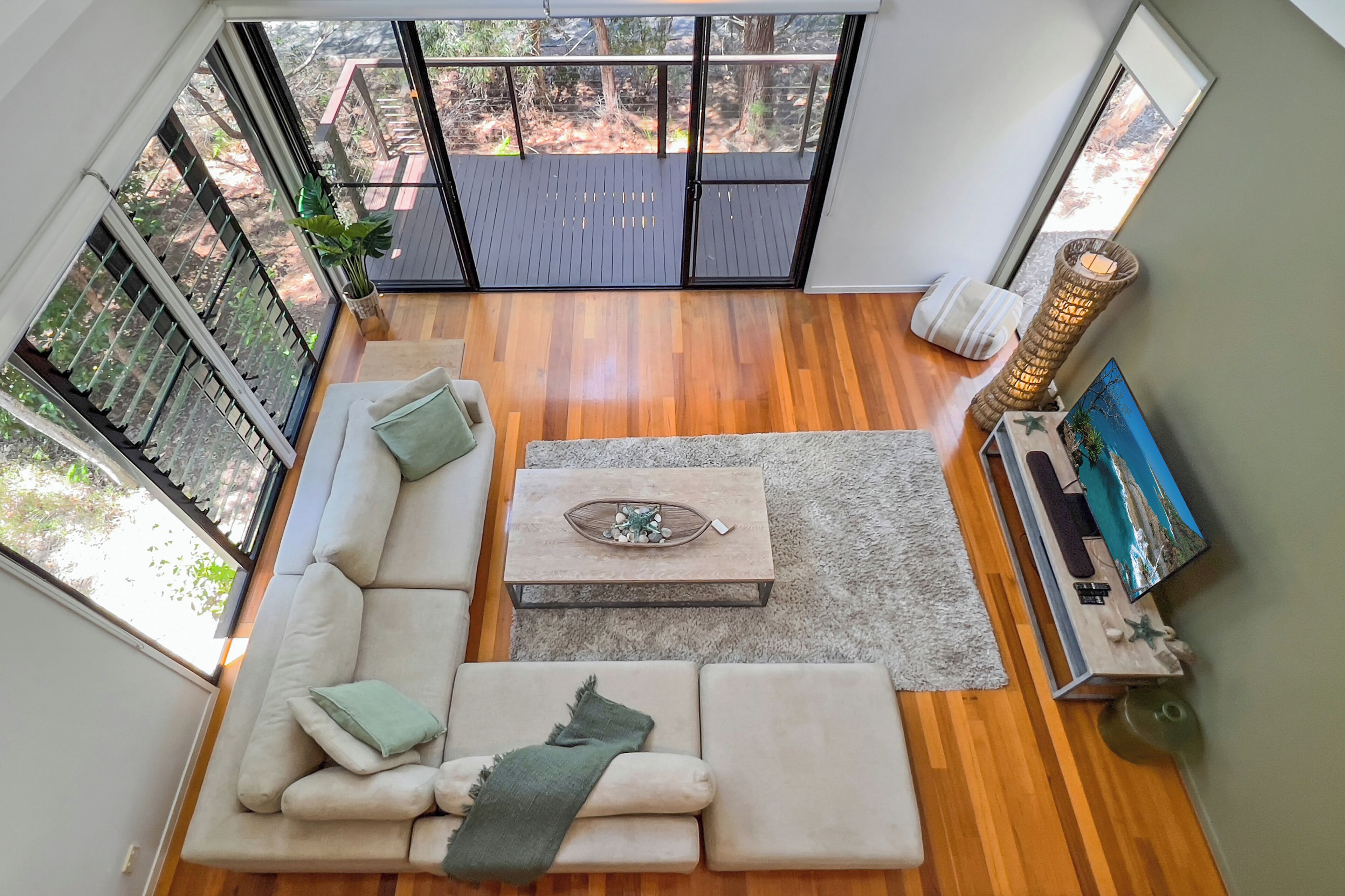 Ein geräumiges Wohnzimmer mit einer großen Glasschiebetür, die auf eine Terrasse im Freien führt, ein beiges Sofa mit Kissen, ein Couchtisch und ein dekorativer Teppich.