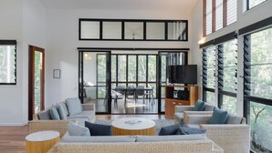 A spacious living area with a high ceiling, large windows, and a modern interior design.