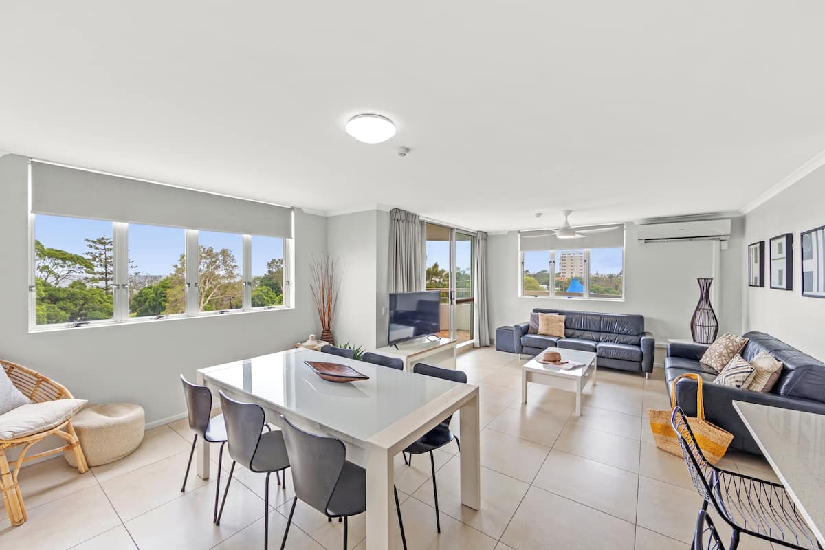 A spacious living room with a dining area, large windows, and a balcony.