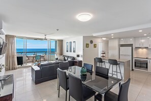 A modern apartment with a dining area, kitchen, and a balcony with a view of the sea.