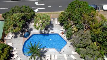 Vista aérea de una piscina rodeada de sillas de descanso y árboles.