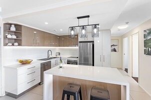Uma cozinha moderna com armários brancos, eletrodomésticos de aço inoxidável e uma ilha central com banquetas.