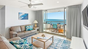A modern living room with a sofa, coffee table, and a view of the ocean through large sliding doors.