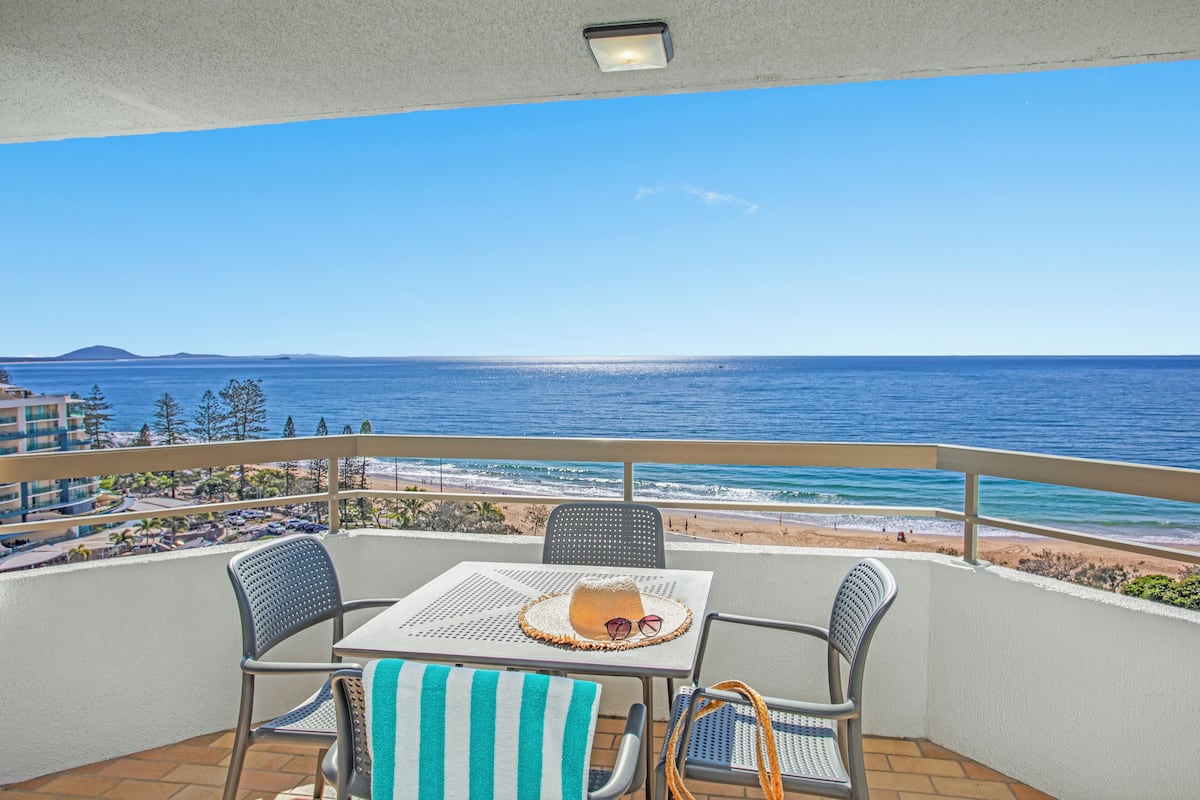 A balcony with a table, chairs, and a view of the ocean.