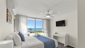A hotel room with a bed, a ceiling fan, a TV, a desk, and a view of the ocean.
