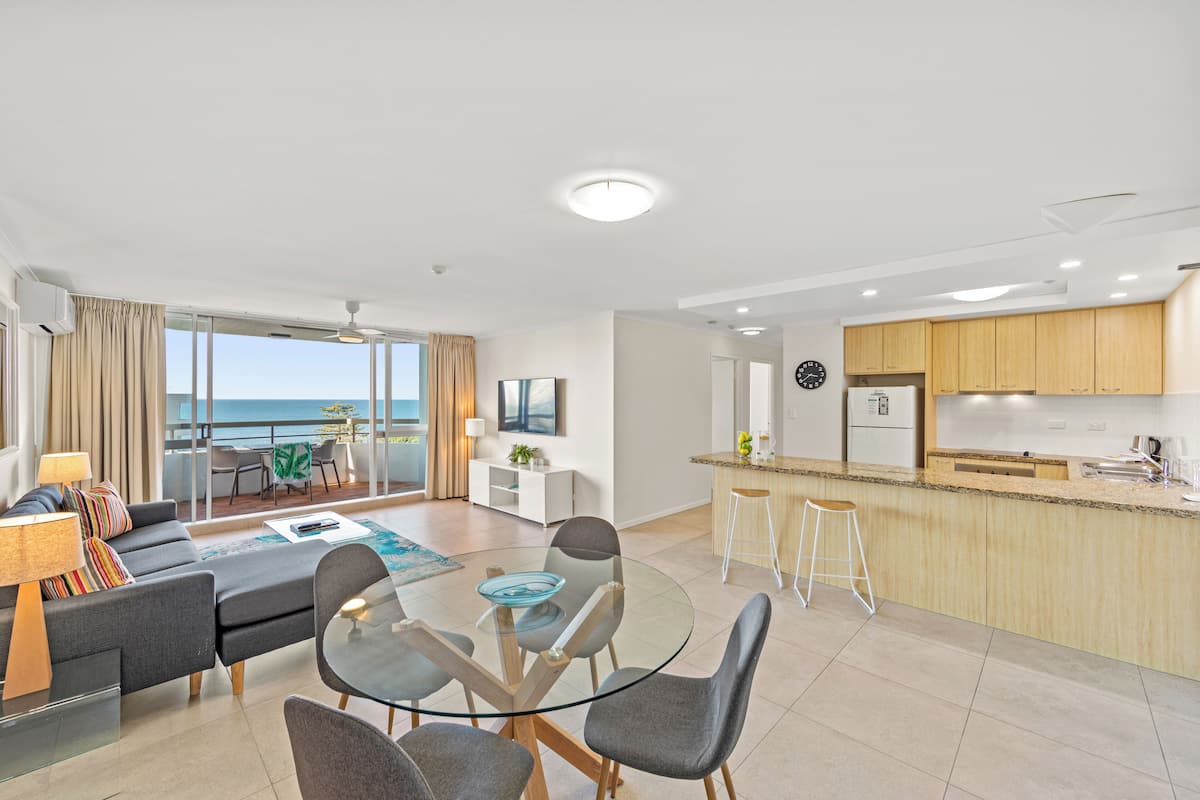 A modern apartment with a dining area, kitchen, and a balcony with a view of the sea.